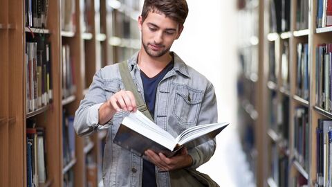 Student mit Buch in der Hand steht in Bibliothek